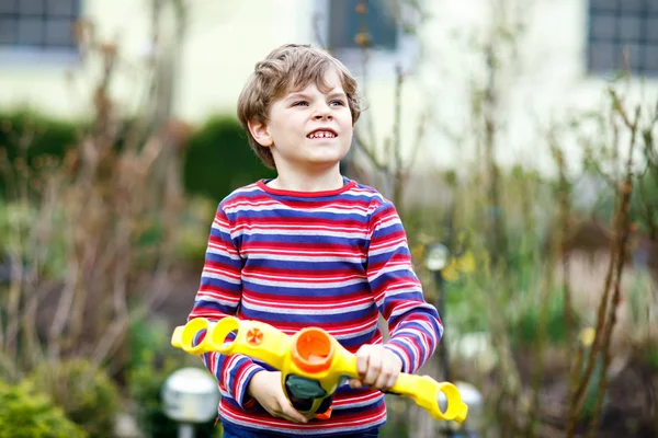 Un ragazzino che gioca con la pistola ad acqua nel giardino primaverile. Studentessa avendo divertimento e azione . — Foto Stock