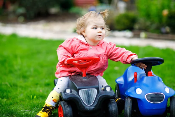 Petite fille mignonne jouant avec deux voitures jouet dans le jardin. Adorable tout-petit enfant qui s'amuse. Fille en vêtements de mode colorés . — Photo