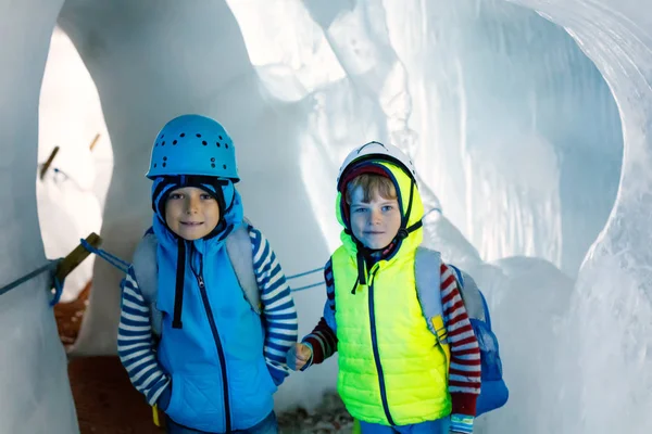Two little boys with safety helmets and clothing with mountains landscape backgrounds. Kids hiking and discovering glacier in Tirol, Austria, Hintertux — Stock Photo, Image