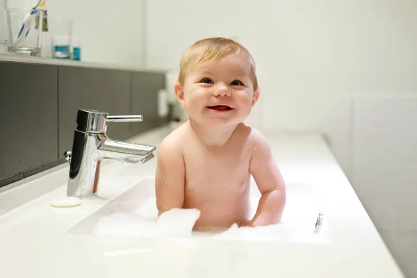 Bebê adorável bonito tomando banho na pia de lavagem e brincando com água e espuma — Fotografia de Stock