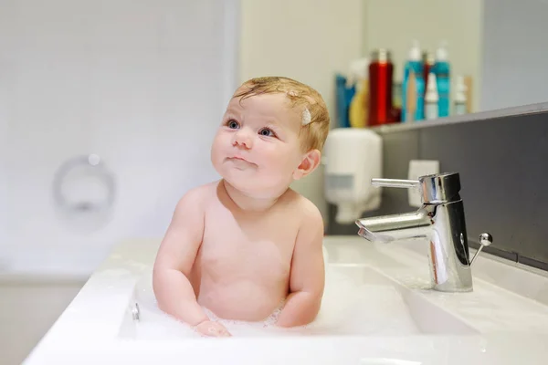 Lindo bebé adorable tomando baño en lavabo y jugando con agua y espuma —  Fotos de Stock