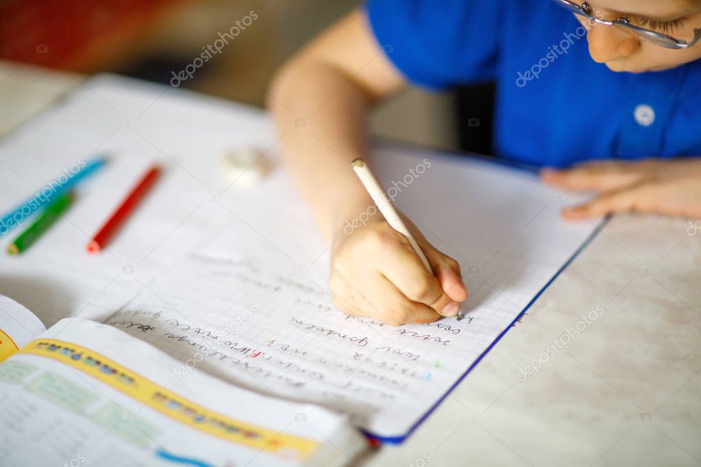 Close-up of little kid boy with glasses at home making homework, writing letters with colorful pens.