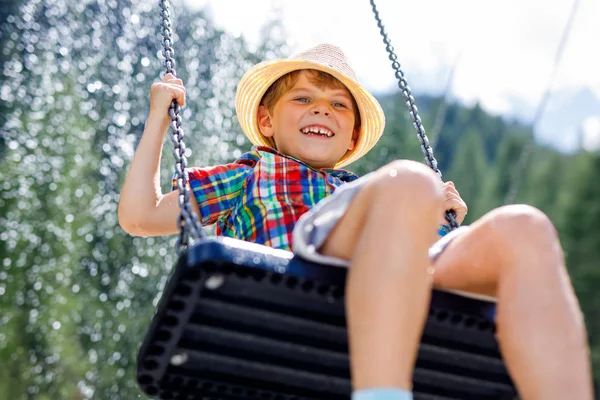 Lustiger kleiner Junge hat Spaß mit Kettenschaukel auf Spielplatz im Freien, während er nass mit Wasser bespritzt wird — Stockfoto