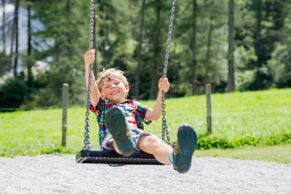 Lustiger kleiner Junge hat Spaß mit Kettenschaukel auf Spielplatz im Freien, während er nass mit Wasser bespritzt wird — Stockfoto