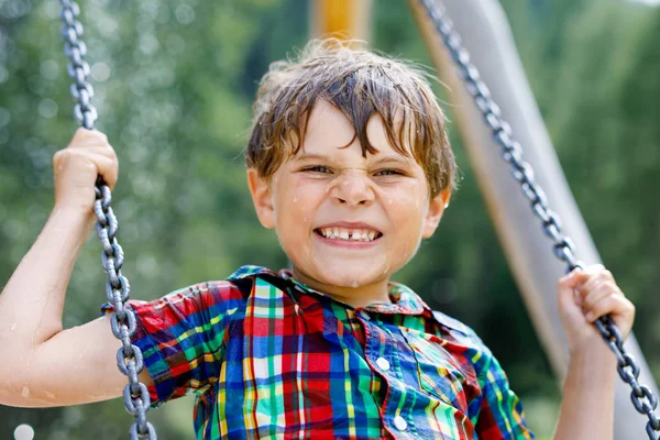Funny kid boy having fun with chain swing on outdoor playground while being wet splashed with water — Stock Photo, Image