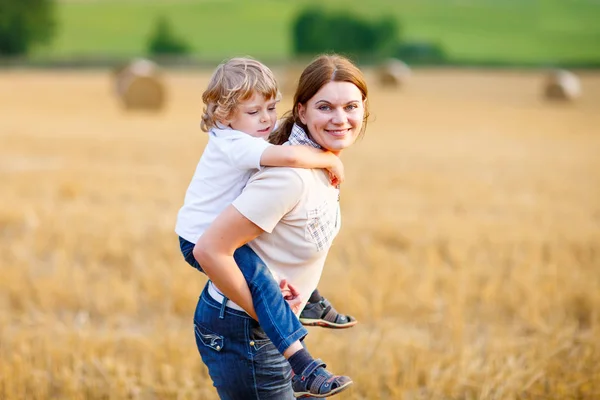 Mother holding kid boy on arms on wheat field in summer — Stock Photo, Image