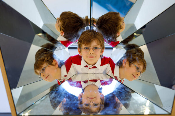 Little kid boy having fun with experiments with mirrors in a musem. Portrait of happy smiling school child.