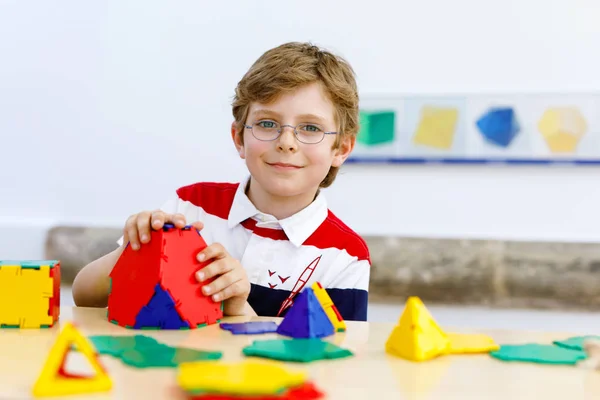 Щасливий хлопчик в окулярах розважається з будівництвом і створює геометричні фігури, вивчає математику і геометрію — стокове фото