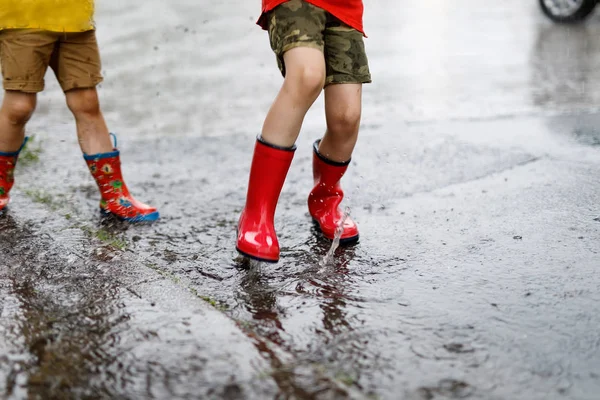 Zwei Kinder in roten Regenstiefeln springen in eine Pfütze. — Stockfoto