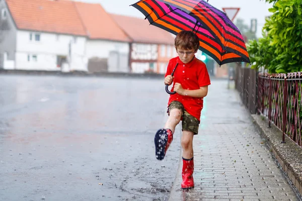 Junge trägt rote Regenstiefel und geht mit Regenschirm — Stockfoto