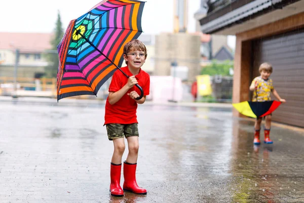 Jongen jongen dragen rode regen laarzen en wandelen met paraplu — Stockfoto