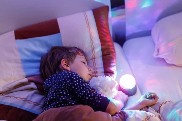 Pequeño niño preescolar durmiendo en la cama con lámpara de colores . — Foto de Stock