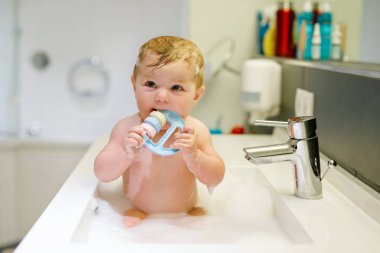 Lavaboda yıkanan, su ve köpükle oynayan sevimli bir bebek.