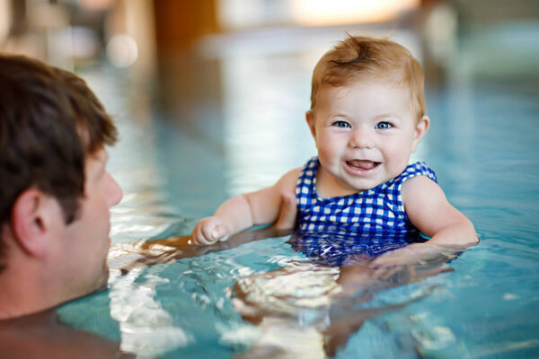 Happy middle-aged father swimming with cute adorable baby girl in swimming pool.