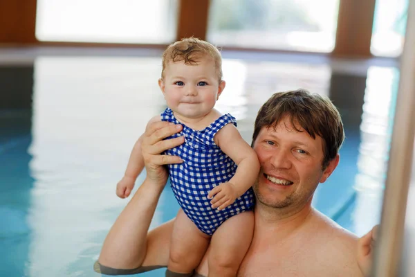Happy middle-aged father swimming with cute adorable baby girl in swimming pool.