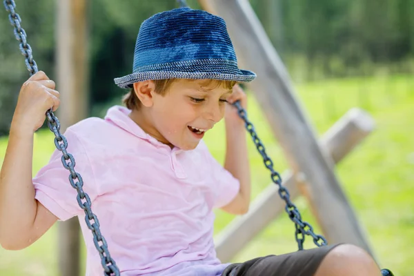 Funny kid boy having fun with chain swing on outdoor playground while being wet splashed with water — Stock Photo, Image