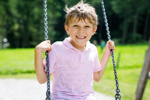 Funny kid boy having fun with chain swing on outdoor playground while being wet splashed with water — Stock Photo, Image