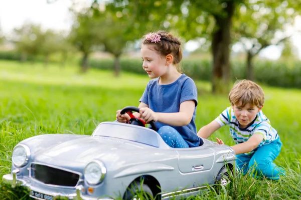 Deux enfants heureux jouent avec une grande vieille voiture jouet dans le jardin d'été, en plein air — Photo