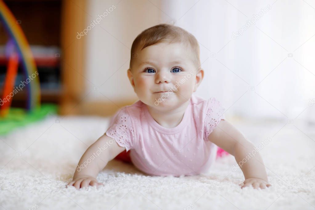 Portrait of baby girl in white sunny bedroom. Newborn child learning crawling.