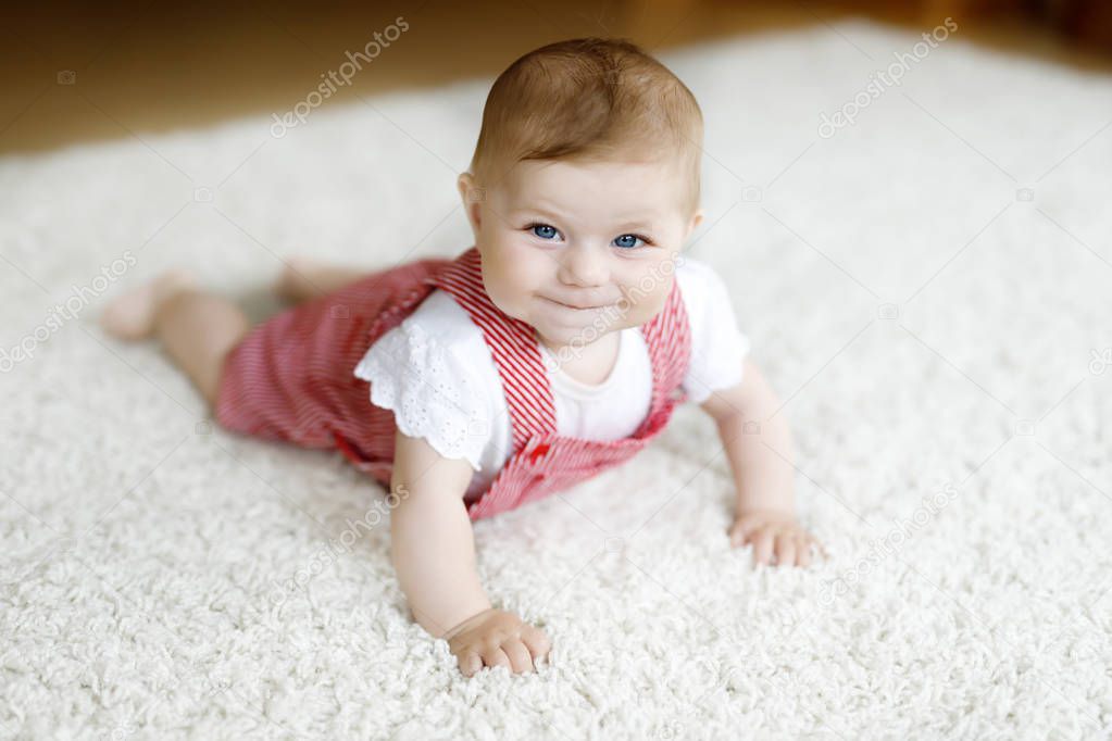 Portrait of baby girl in white sunny bedroom. Newborn child learning crawling.