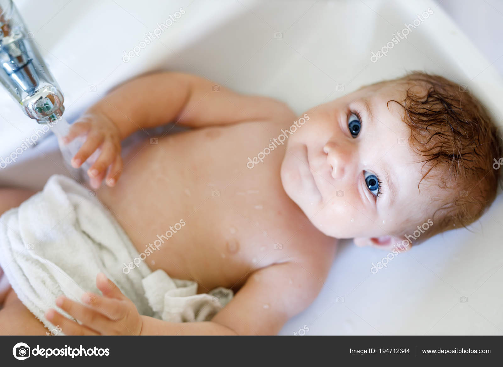 Cute adorable baby taking bath in washing sink and grab water tap