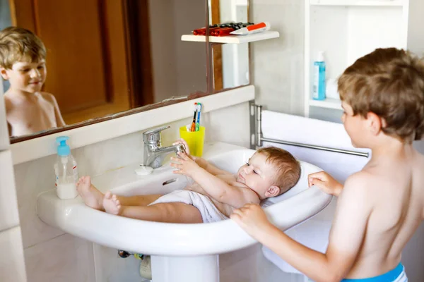 Cute adorable baby taking bath in washing sink and grab water tap. — Stock Photo, Image