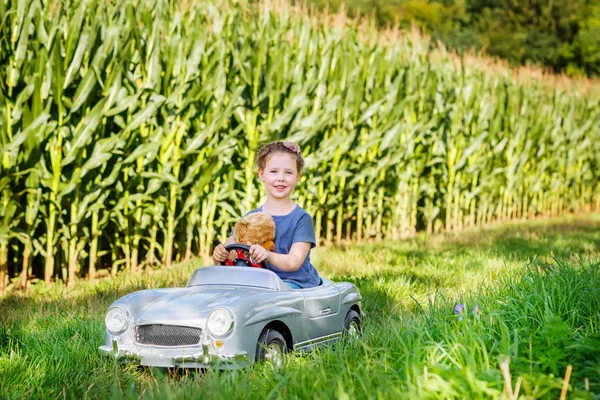 Little preschool kid girl driving big toy car and having fun with playing with big plush toy bear — Stock Photo, Image