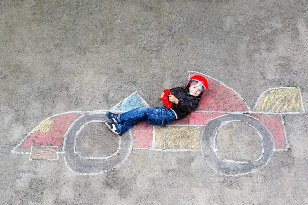 Schattig kind jongetje tekenen met kleurrijke krijtjes race auto foto op asfalt. — Stockfoto