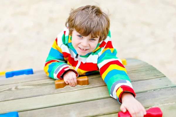 Niño rubio feliz divirtiéndose y escalando en el patio al aire libre. Divertido niño alegre sonriendo y haciendo deportes. Vacaciones de verano, primavera y otoño para niños activos. Niño en ropa de moda colorida . —  Fotos de Stock