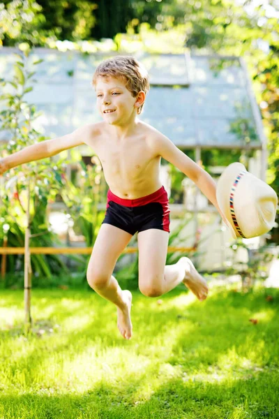 Söta aktiv unge pojke hoppar i trädgården på varma soliga sommardag. Lycklig unge tittar på kameran. Bedårande barn med blont hår och blå ögon — Stockfoto