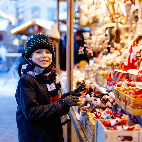 Pequeno garoto bonito menino selecionando decoração no mercado de Natal. Bonita criança compras de brinquedos e ornamentos decorativos coisas para a árvore. Mercado de Natal na Alemanha. — Fotografia de Stock