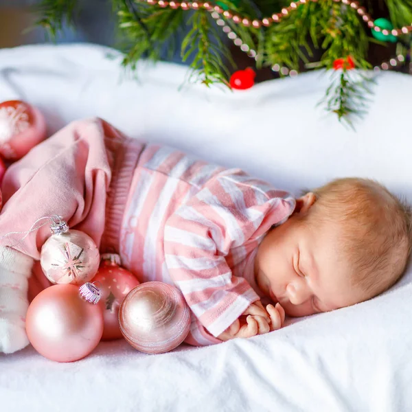 Bebé recién nacido de una semana con bolas rosadas cerca del árbol de Navidad con luces de guirnalda de colores en el fondo. Primer plano de niño lindo, niña durmiendo. Familia, Navidad, nacimiento, nueva vida — Foto de Stock