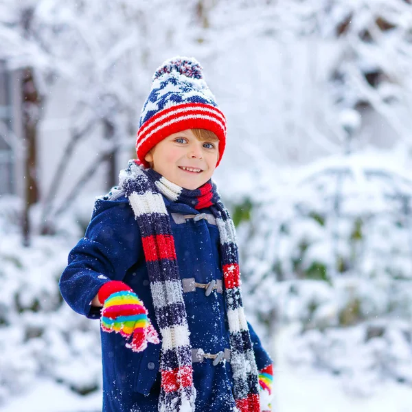 Menino pré-escolar em roupas coloridas brincando ao ar livre durante a forte queda de neve. Lazer ativo com crianças no inverno em dias nevados frios. Criança feliz se divertindo, brincando com neve. Moda de inverno. — Fotografia de Stock