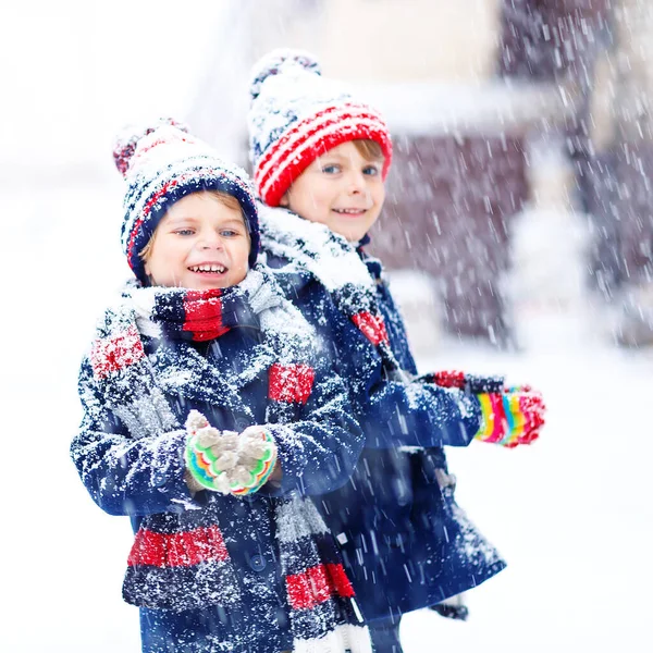Two little kid boys in colorful fashion clothes playing outdoors during strong snowfall. Active leisure with children in winter on cold days. Happy siblings and friends having fun with first snow. — Stock Photo, Image