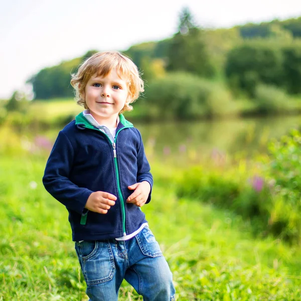 Little blond kid boy playing near forest lake on summer evening. cute child with curly hairs playing. Family on weekend or vacations — Stock Photo, Image