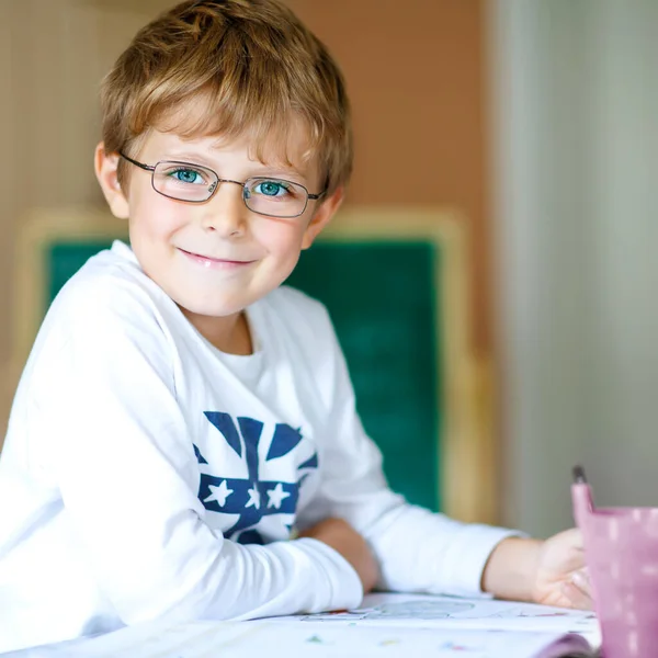 Retrato de lindo niño de la escuela feliz con gafas en casa haciendo tarea. Niño pequeño escribiendo con lápices de colores, en el interior. Escuela primaria y educación .. —  Fotos de Stock