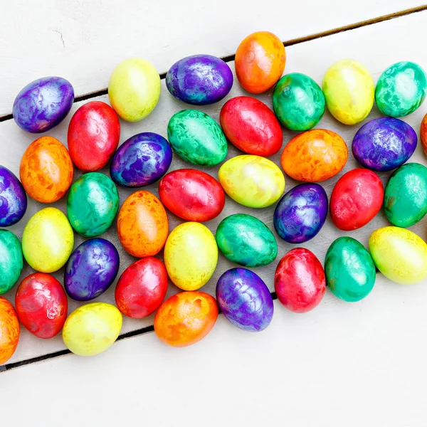 Huevos de Pascua sobre fondo de madera. Huevos coloridos en diferentes colores rojo, amarillo, naranja, púrpura y verde. Vieja tradición para las vacaciones. Primer plano de muchos huevos . — Foto de Stock