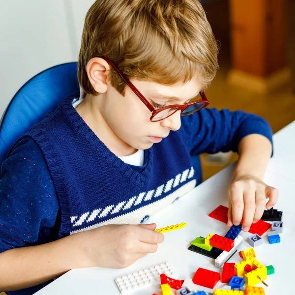 Petit enfant blond avec des lunettes jouant avec beaucoup de blocs en plastique coloré. Adorable écolier qui s'amuse avec la construction et la création de robots. Loisirs créatifs technique moderne et robotique. — Photo