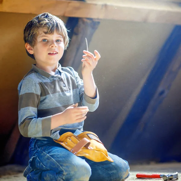 Kleiner Junge hilft mit Spielzeug auf Baustelle. Lustiges Kind von 6 Jahren, das Spaß am Bau eines neuen Familienhauses hat. Kind mit Nägeln und Hammer hilft Vater bei Renovierung von altem Haus. — Stockfoto