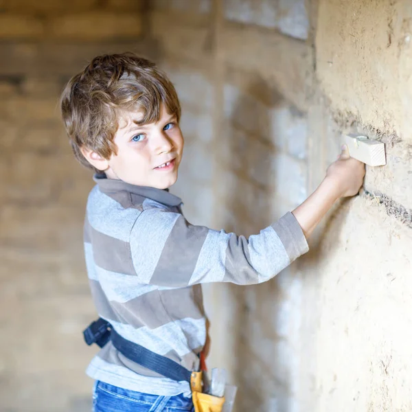 Ragazzino che aiuta con gli attrezzi giocattolo sul cantiere. Bambino divertente di 6 anni che si diverte a costruire una nuova casa di famiglia. Ragazzo con chiodi e martello che aiuta il padre a ristrutturare la vecchia casa. — Foto Stock