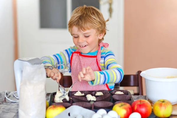 Bonito pequeno menino pré-escolar loiro feliz cozinhando bolo de maçã e muffins na cozinha doméstica. Engraçado adorável criança saudável se divertindo com o trabalho com misturador, farinha, ovos, frutas. Pequeno ajudante dentro de casa — Fotografia de Stock