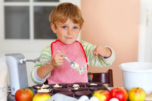 可爱的金发学龄前小男孩在自家厨房里烤苹果蛋糕和松饼。有趣可爱的健康的孩子与搅拌机，面粉，鸡蛋，水果一起工作的乐趣。家里的小帮手 — 图库照片