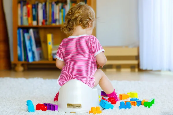 Closeup of cute little 12 months old toddler baby girl child sitting on potty. Kid playing with educational wooden toy. Toilet training concept. Baby learning, development steps
