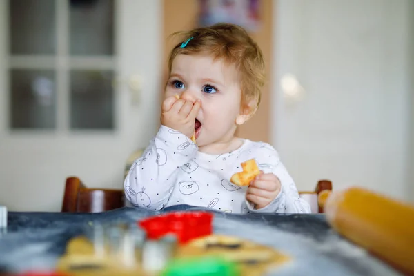 Bonito menina fazendo biscoitos de Natal de gengibre em casa. Adorável loira feliz criança saudável se divertindo na cozinha doméstica. Lazer tradicional com crianças no Natal. Massa de degustação de crianças . — Fotografia de Stock