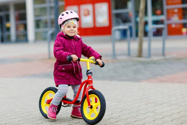 ランバランスバイクに乗って安全ヘルメットに乗ってかわいい幼児の女の子。リーン自転車で学ぶ楽しさを持つ幸せな健康的な素敵な赤ちゃんの子供。屋外で寒い日にアクティブな子供. — ストック写真