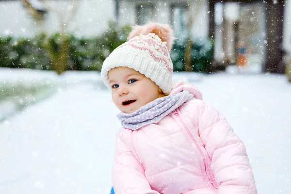 Cute little toddler girl enjoying a sleigh ride on snow. Child sledding. Baby kid riding a sledge in colorful fashion clothes. Outdoor active fun for family winter vacation on day with snowfall — Stock Photo, Image