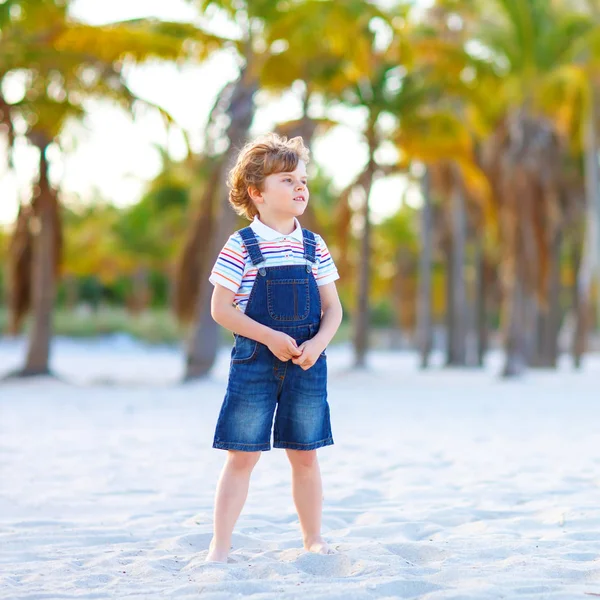 Uroczy, aktywny chłopiec bawiący się na plaży w Miami, Key Biscayne. Happy cute dziecko relaks, gry z piaskiem i korzystających słoneczny ciepły dzień w pobliżu palm i oceanu — Zdjęcie stockowe