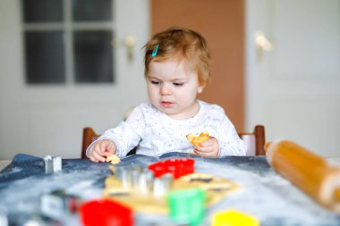 Evde zencefilli Noel kurabiyesi pişiren tatlı küçük bir kız. Sevimli, mutlu, sağlıklı çocuk ev mutfağında eğleniyor. Yılbaşı zamanı çocuklarla geleneksel bir eğlence. Bebek hamuru tadıyor.