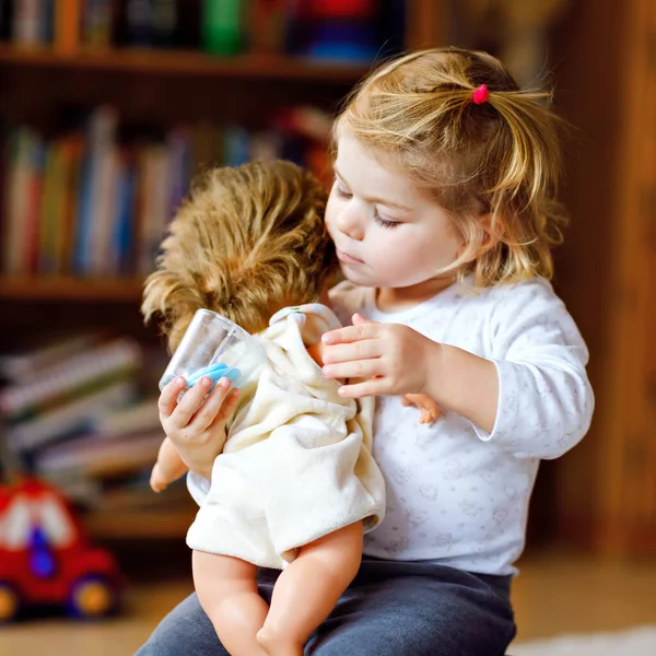 Чарівна мила маленька дівчинка, яка грає з лялькою. Щаслива здорова дитина розважається з рольовою грою, граючи матір вдома або в дитячій кімнаті. Активна дочка з іграшкою — стокове фото