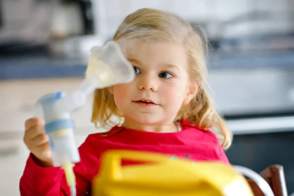 Piccola bambina che fa l'inalazione con il nebulizzatore a casa. Un bambino adorabile che tiene il dispositivo. Bambino che ha influenza e tosse dopo tempo invernale a camera dei bambini. asma inalatore inalazione vapore malato concetto — Foto Stock